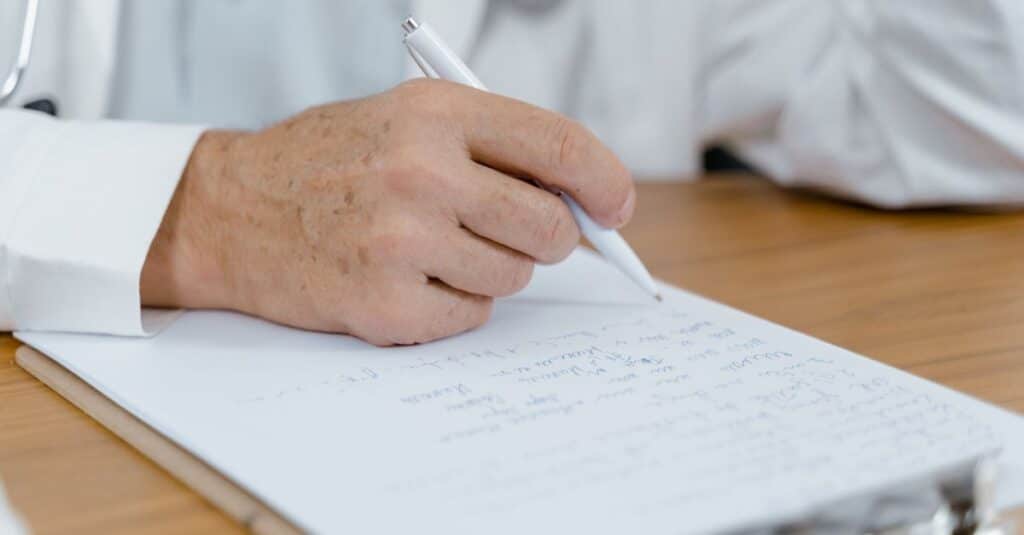 Mão de médico escrevendo anotações em papel durante análise de um laudo de perícia médica