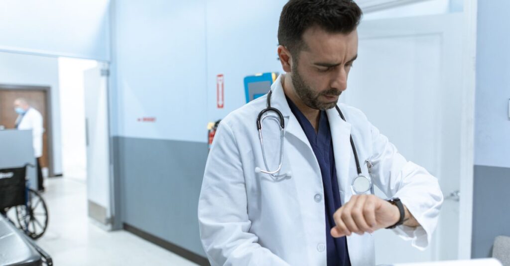 Médico de jaleco branco olha o relógio em corredor de hospital, tema adicional noturno